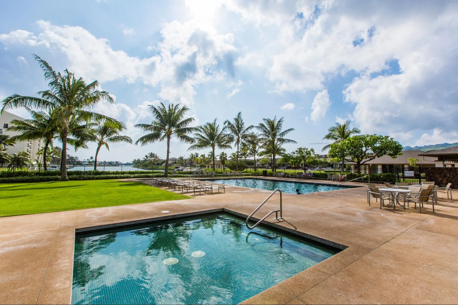 An outdoor swimming pool is surrounded by palm trees and a paved deck.