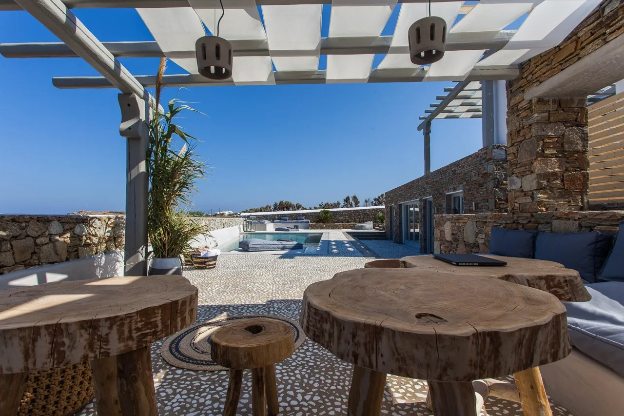 Un patio soleado con asientos rústicos, una pérgola y una piscina.