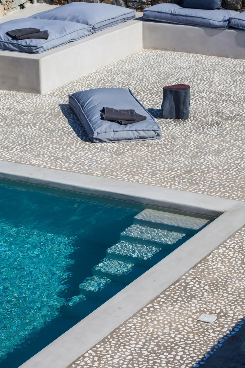 An outdoor pool with cushioned lounging areas on a patterned deck.