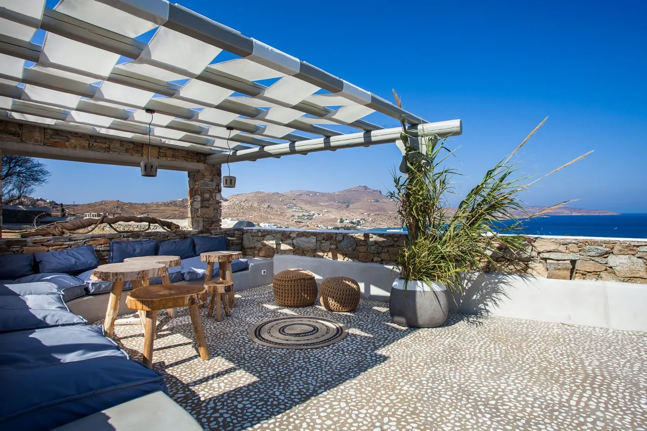Una terraza exterior de piedra tiene asientos acolchados y vistas al mar.