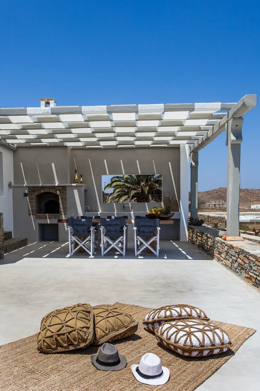 Comedor exterior cubierto con mesa y asientos junto a una parrilla empotrada.