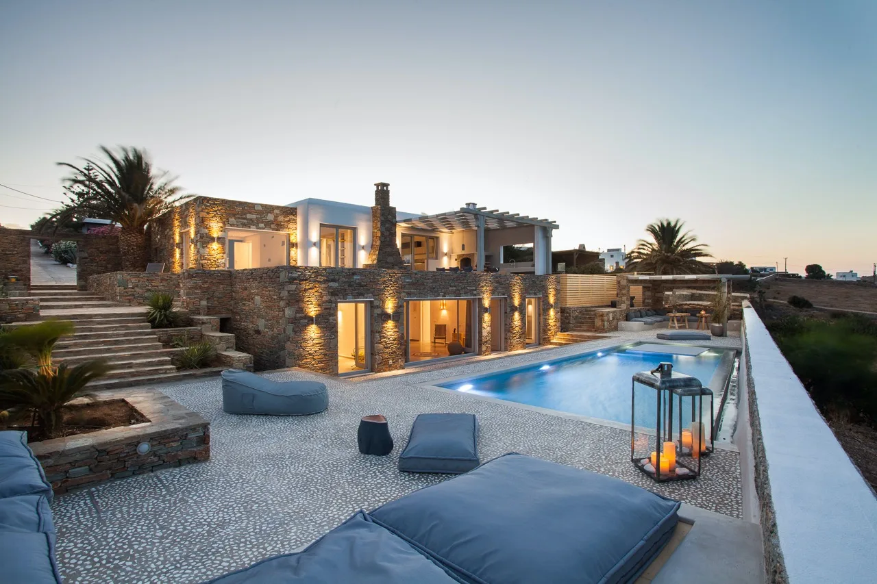 A modern villa opens onto a swimming pool and paved patio.