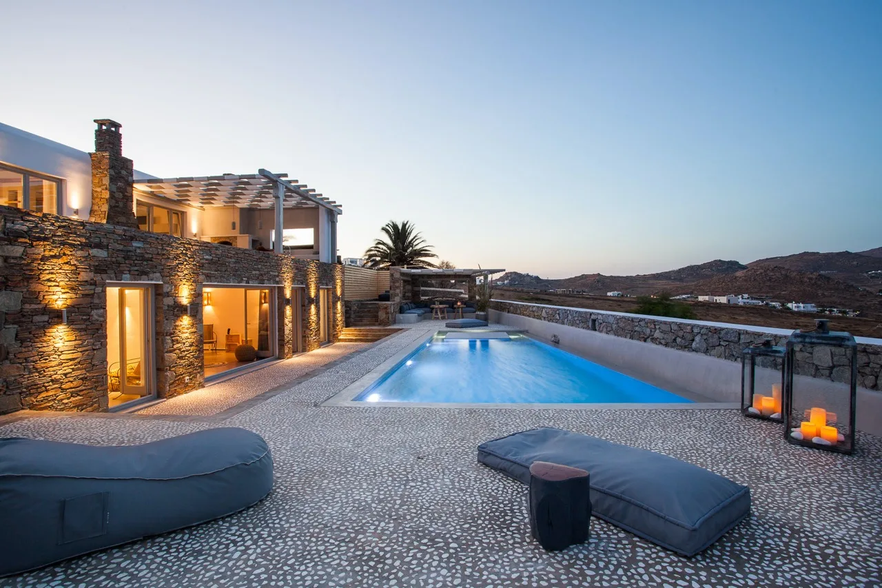 Una villa de piedra iluminada junto a una piscina al anochecer.