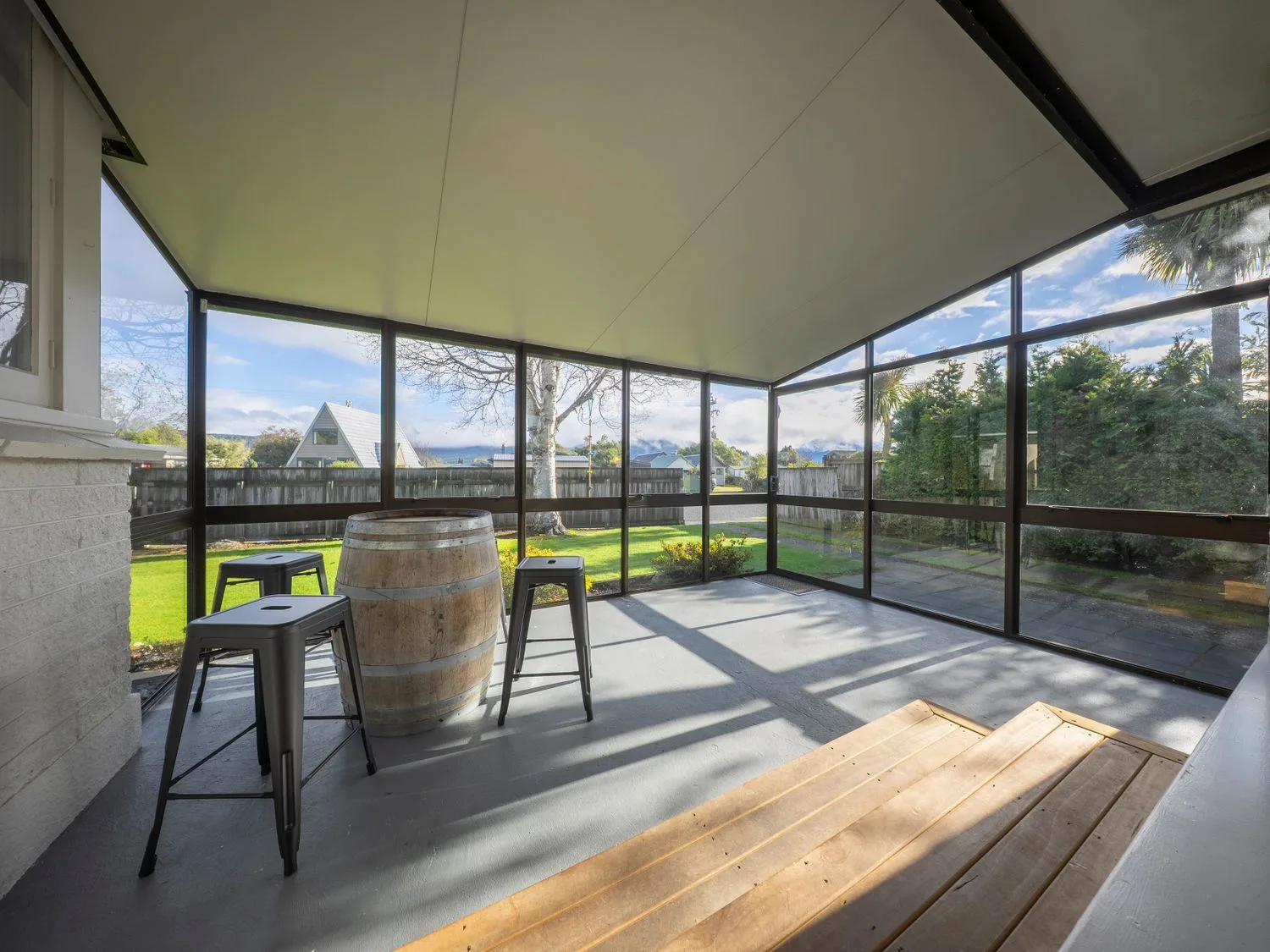 Un patio cubierto con taburetes y un barril de madera junto a grandes ventanas.