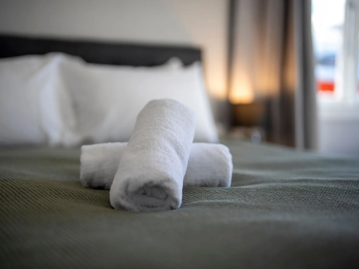Un dormitorio con toallas enrolladas sobre una cama bien tendida.