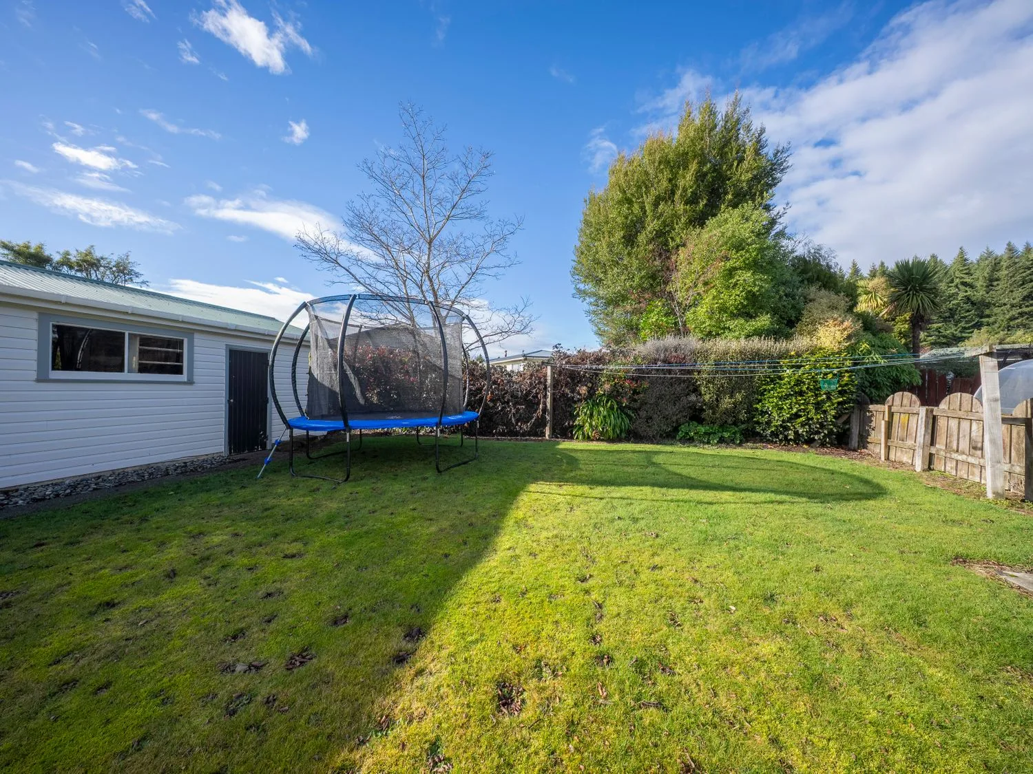 Un jardín con una cama elástica y un cobertizo en Quiet on Quintin - Te Anau Holiday Home, en Te Anau
