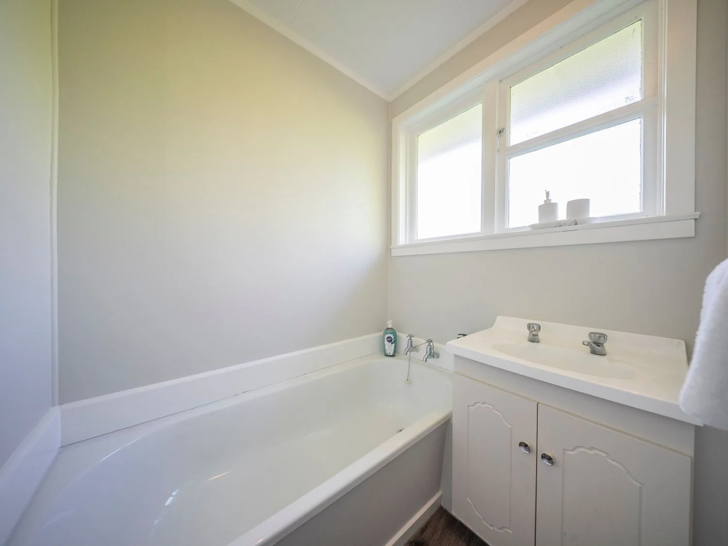 Un baño con bañera y lavabo bajo una ventana.