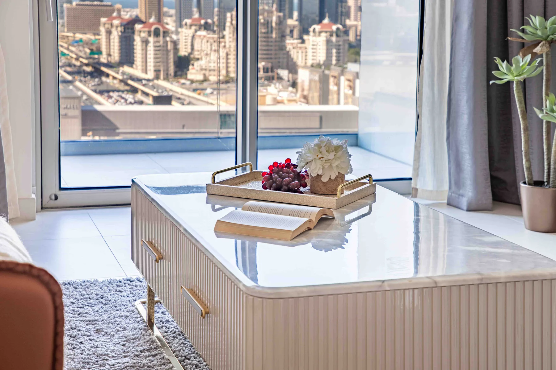 Una sala luminosa con una mesa de centro brillante junto a grandes ventanales con vistas a la ciudad.