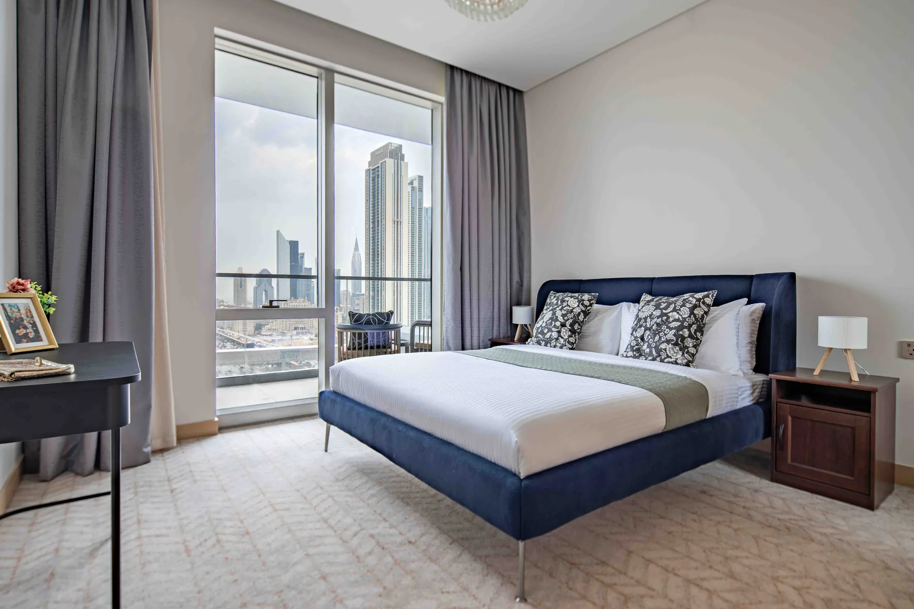 Un dormitorio con una cama junto a ventanales con vistas a edificios de la ciudad.