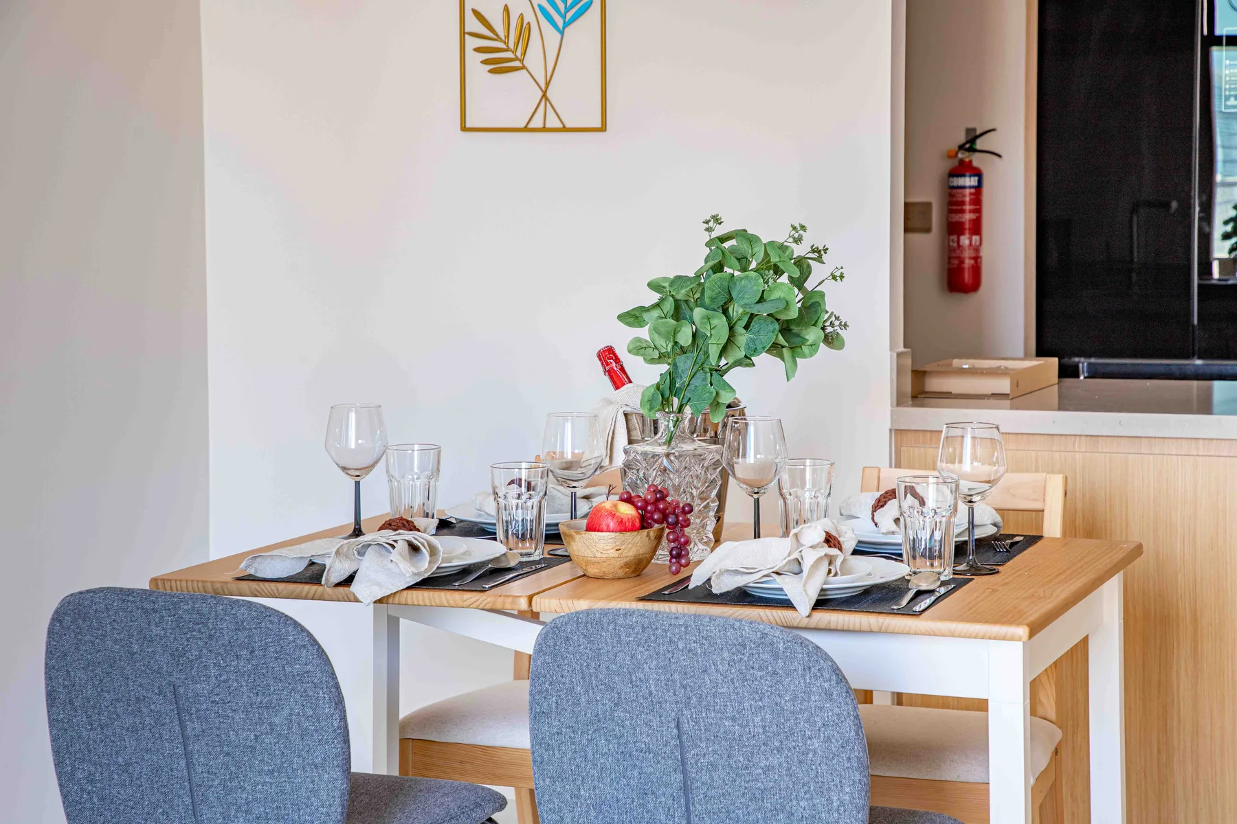 Comedor con la mesa puesta, asientos azules y un centro de mesa frondoso.