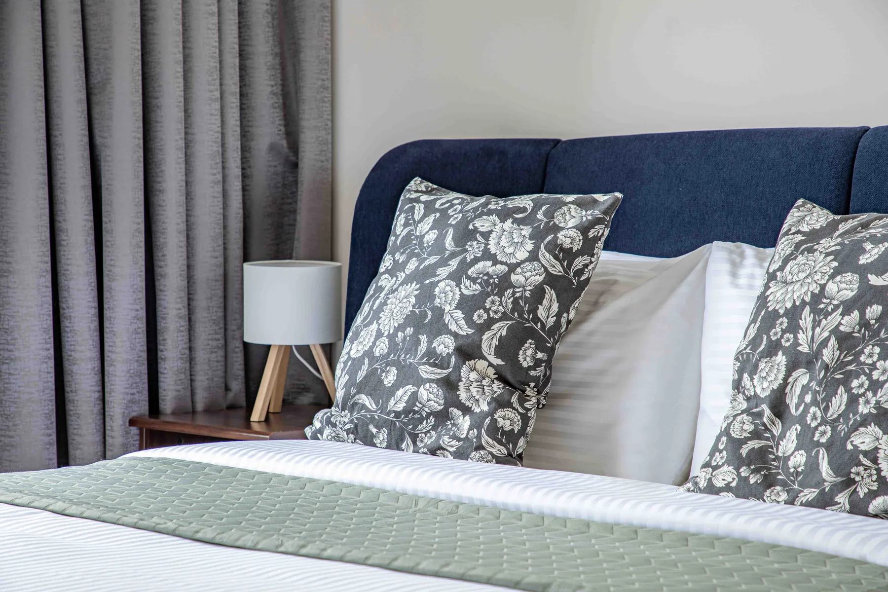 Dormitorio con una cama, almohadas estampadas y cortinas grises.