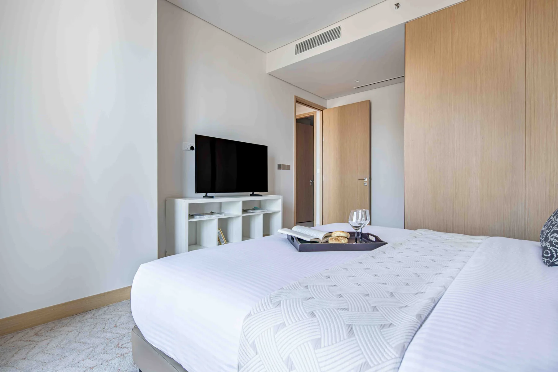Un dormitorio con una cama bien tendida y un televisor sobre un mueble bajo.
