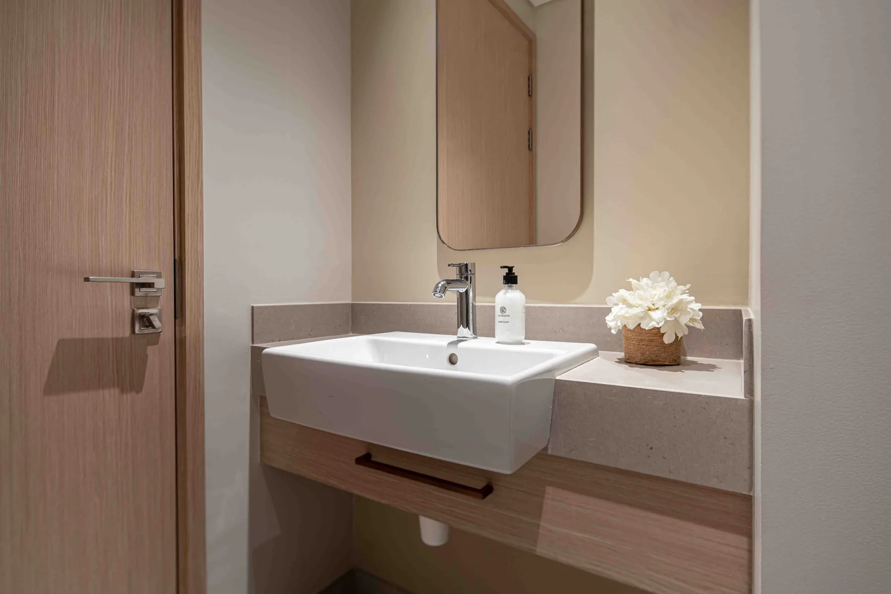 Un lavabo de baño con espejo, grifo y un pequeño arreglo floral.