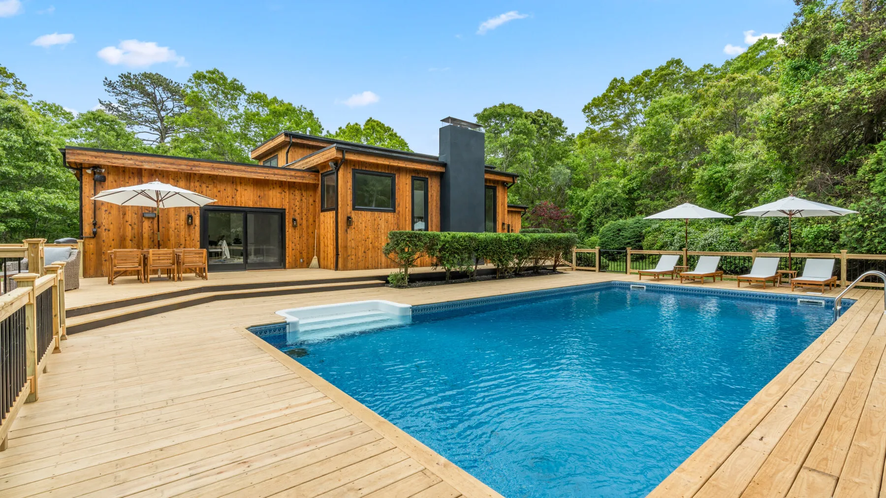 Una piscina al aire libre está junto a una terraza de madera y una casa moderna.