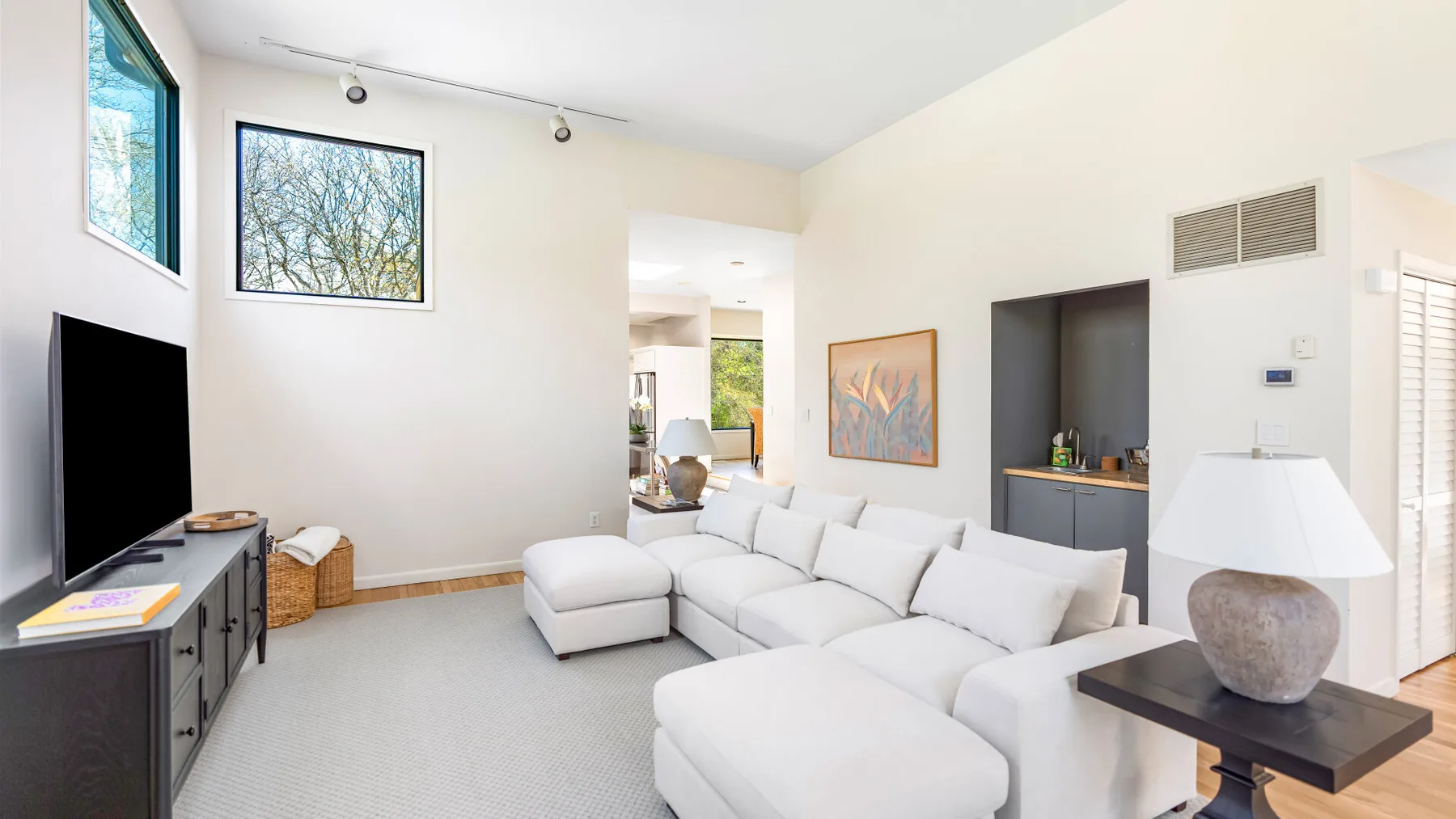 Una sala luminosa con asientos seccionales blancos y un televisor.