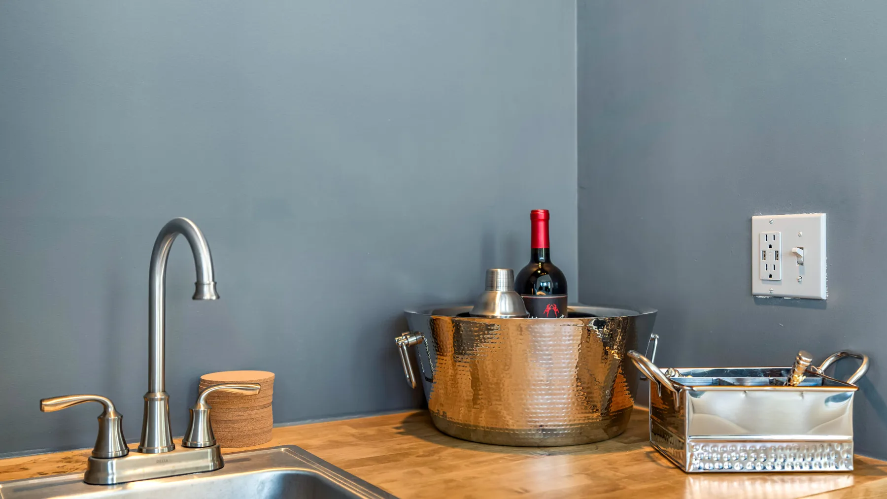 Una encimera de cocina con un grifo, una cubitera y una botella de vino.