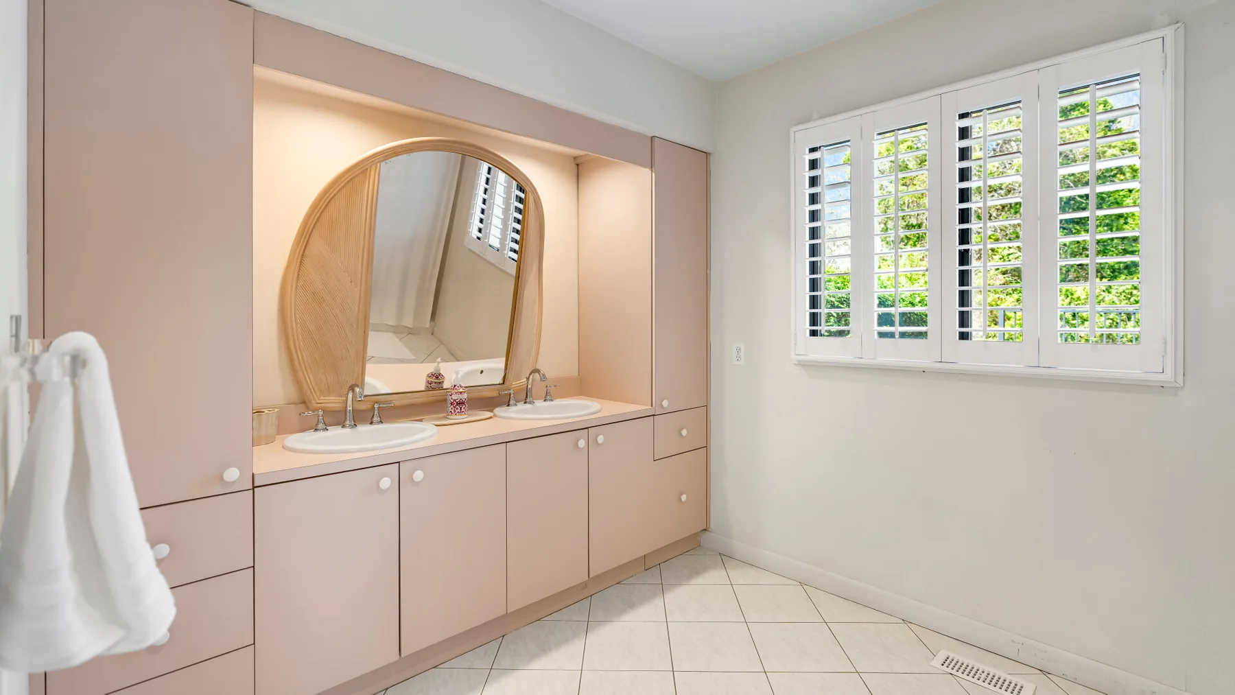 Un tocador de baño con un espejo grande y una ventana con persianas.