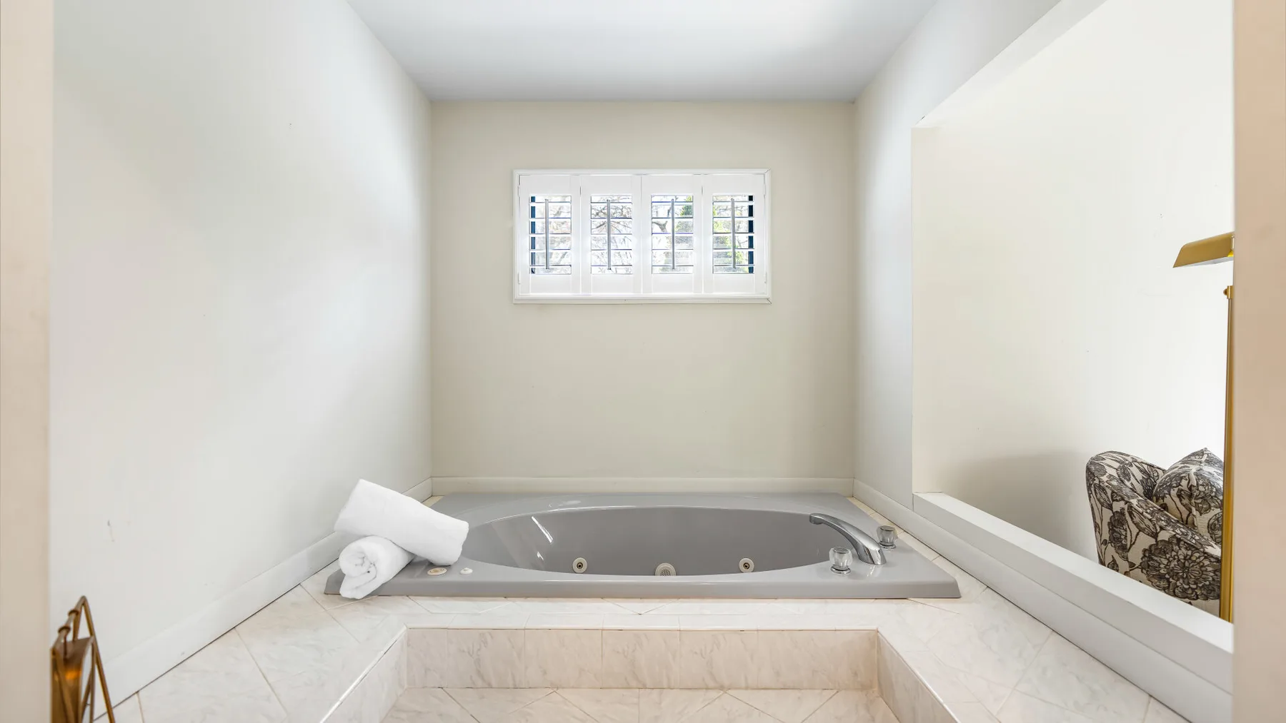 Una bañera empotrada está bajo una ventana pequeña en un baño luminoso.