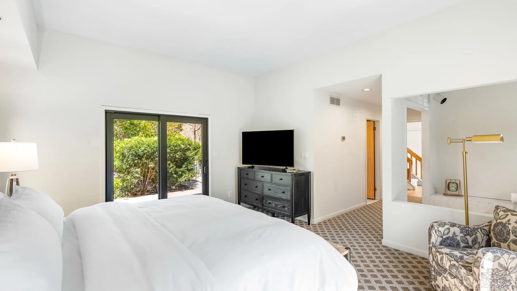 Un dormitorio luminoso con una cama grande, un televisor y puertas de vidrio con vista a la vegetación.