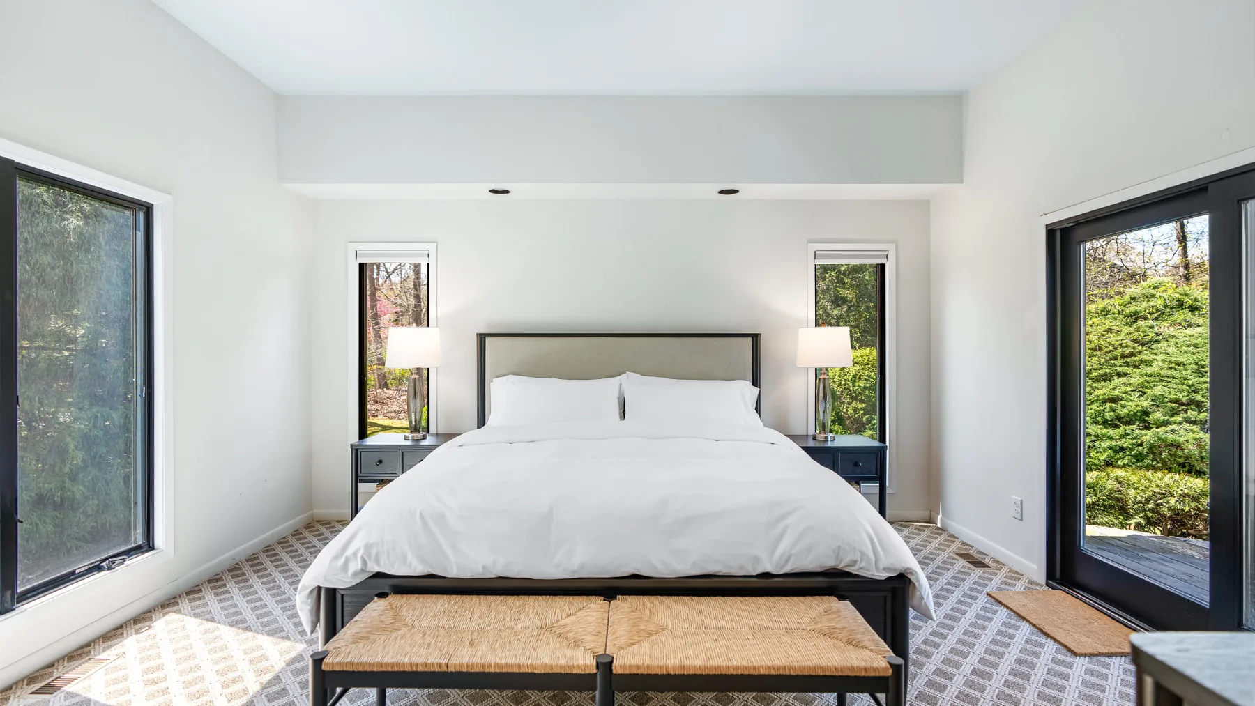 Un dormitorio luminoso con una cama blanca entre ventanas y puertas de vidrio.