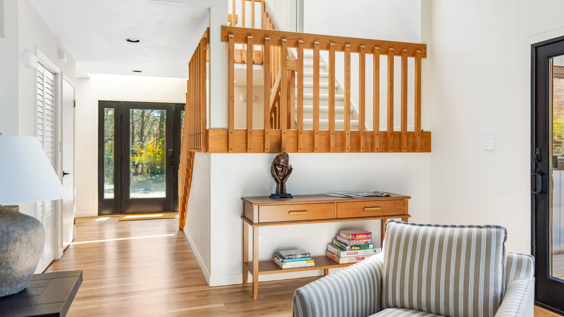 Un pasillo interior luminoso con una escalera de madera y un sillón a rayas.