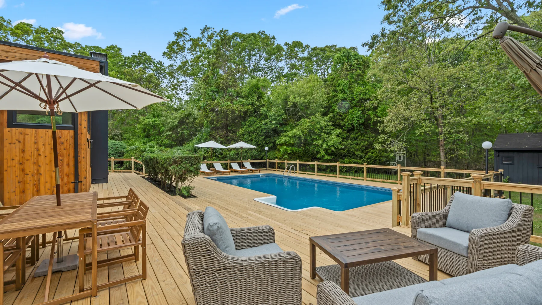 Una piscina al aire libre está junto a una terraza de madera con asientos y sombrillas.