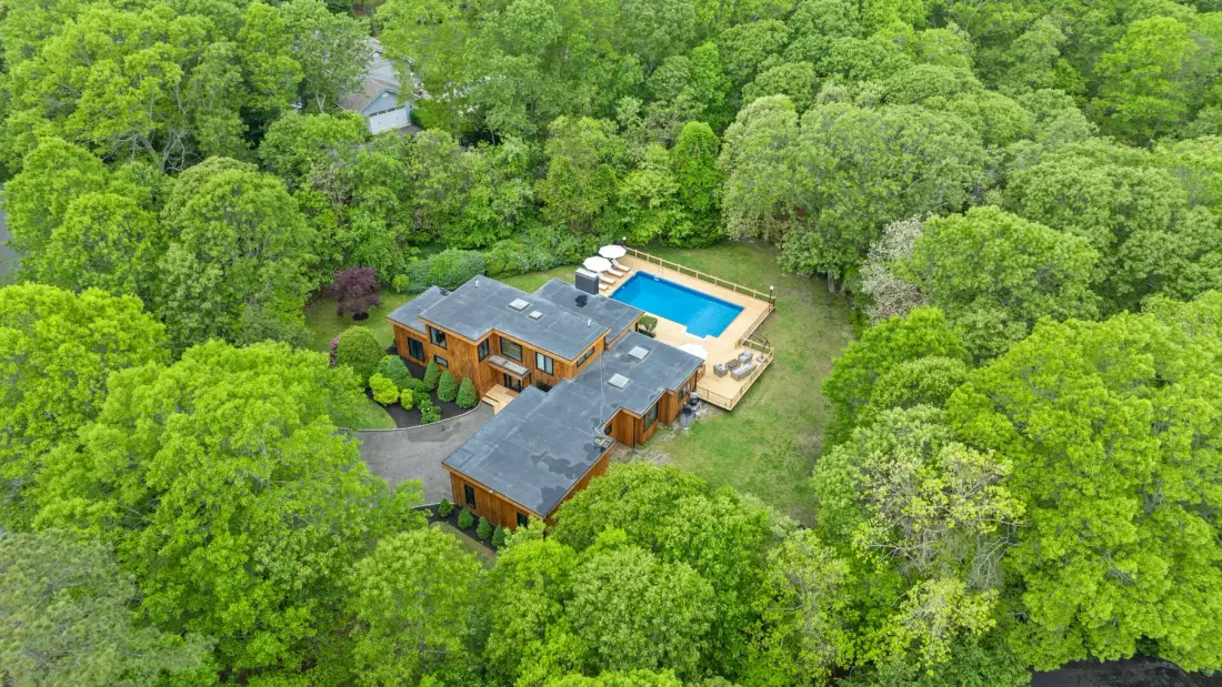 Una vista aérea muestra una casa y una piscina rodeadas de árboles frondosos.