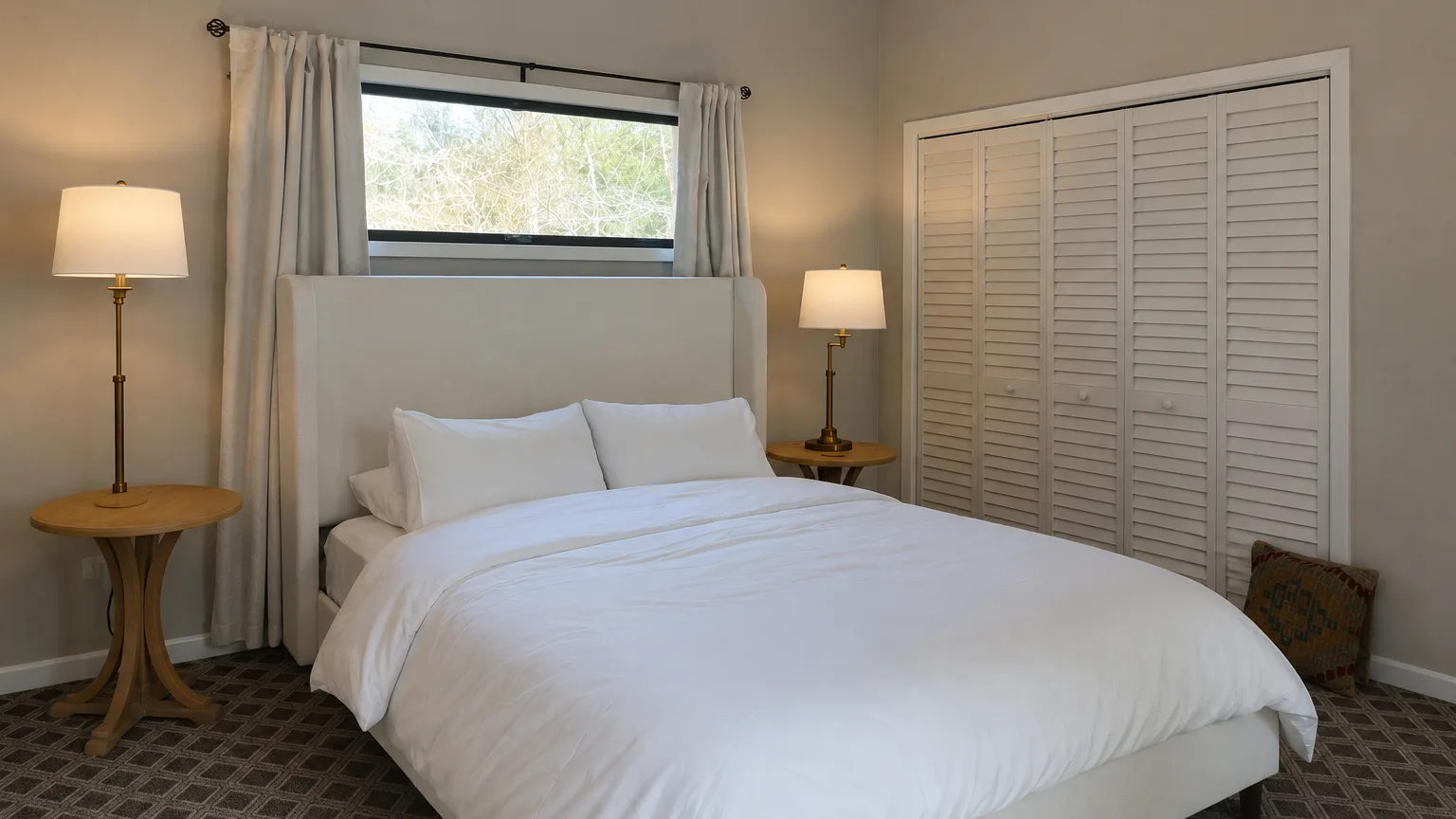 Un dormitorio con una cama bien tendida y una ventana detrás del cabecero.