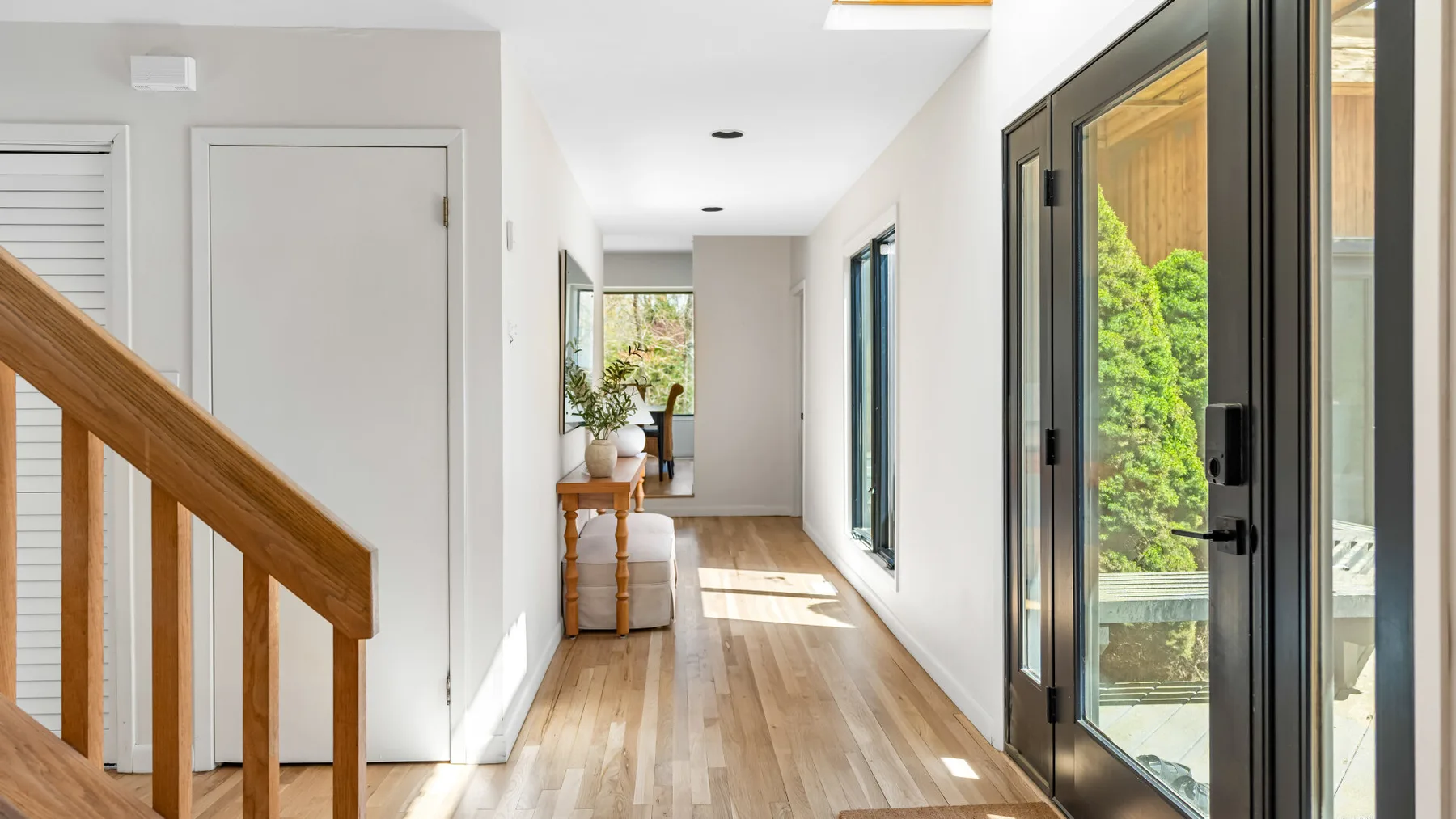 Un pasillo luminoso con suelo de madera y puertas de cristal a un lado.