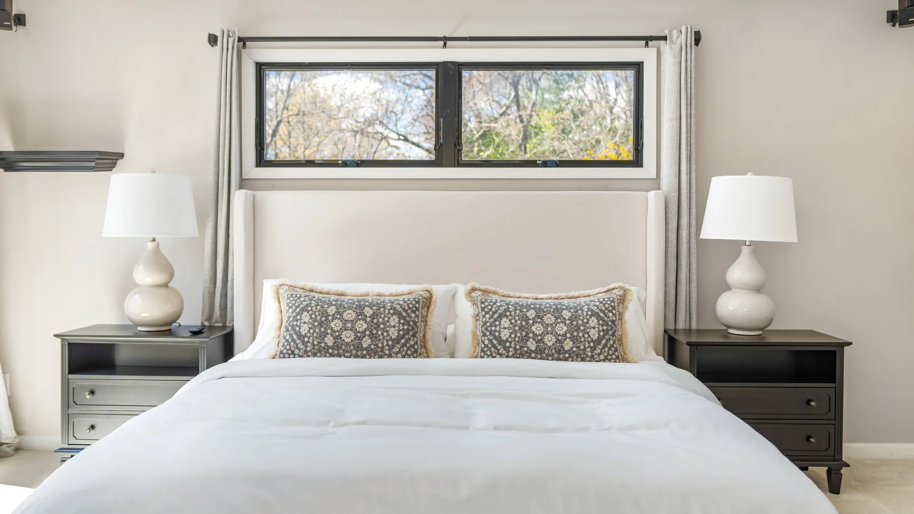 Un dormitorio con una cama bien tendida y una ventana amplia sobre el cabecero.