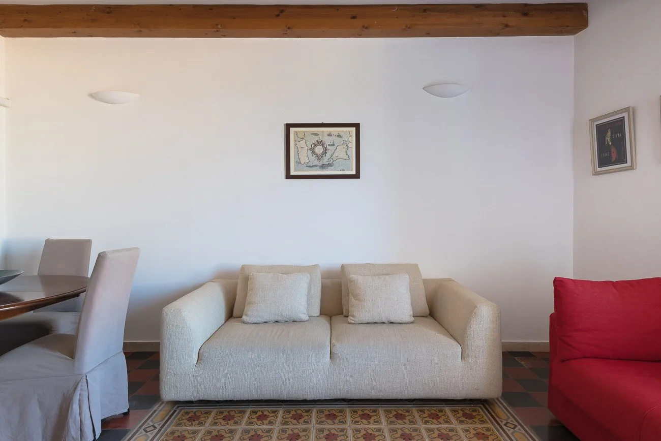 A living room with a light-colored sofa, a red seat, and framed wall art.