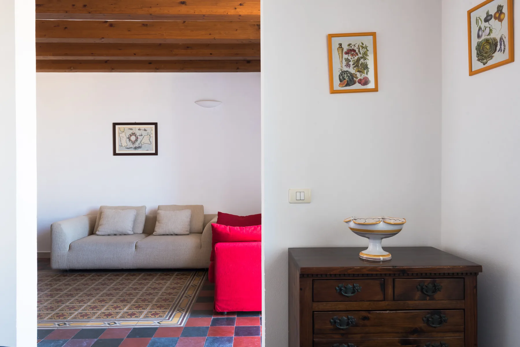 A living room with a sofa, colorful floor tiles, and a wooden chest.