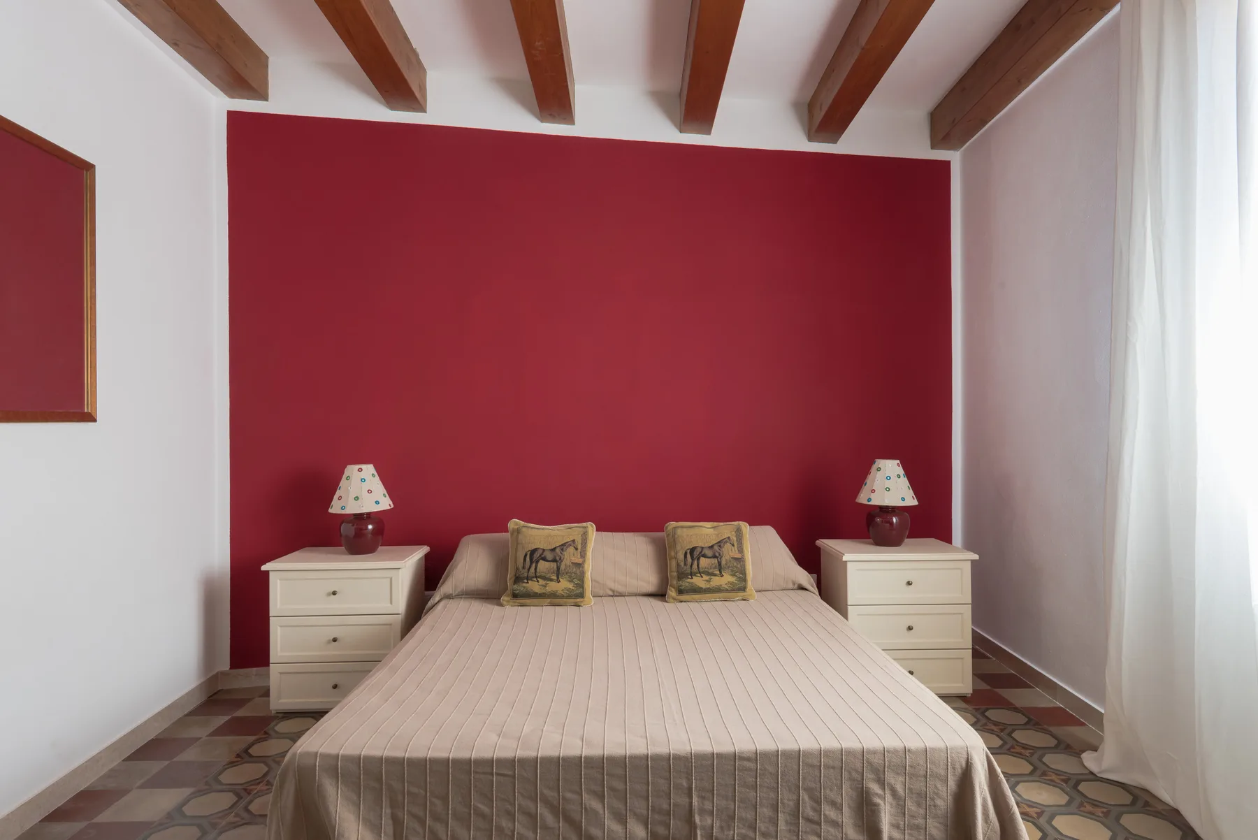 A bedroom with a double bed against a red wall and matching bedside tables.
