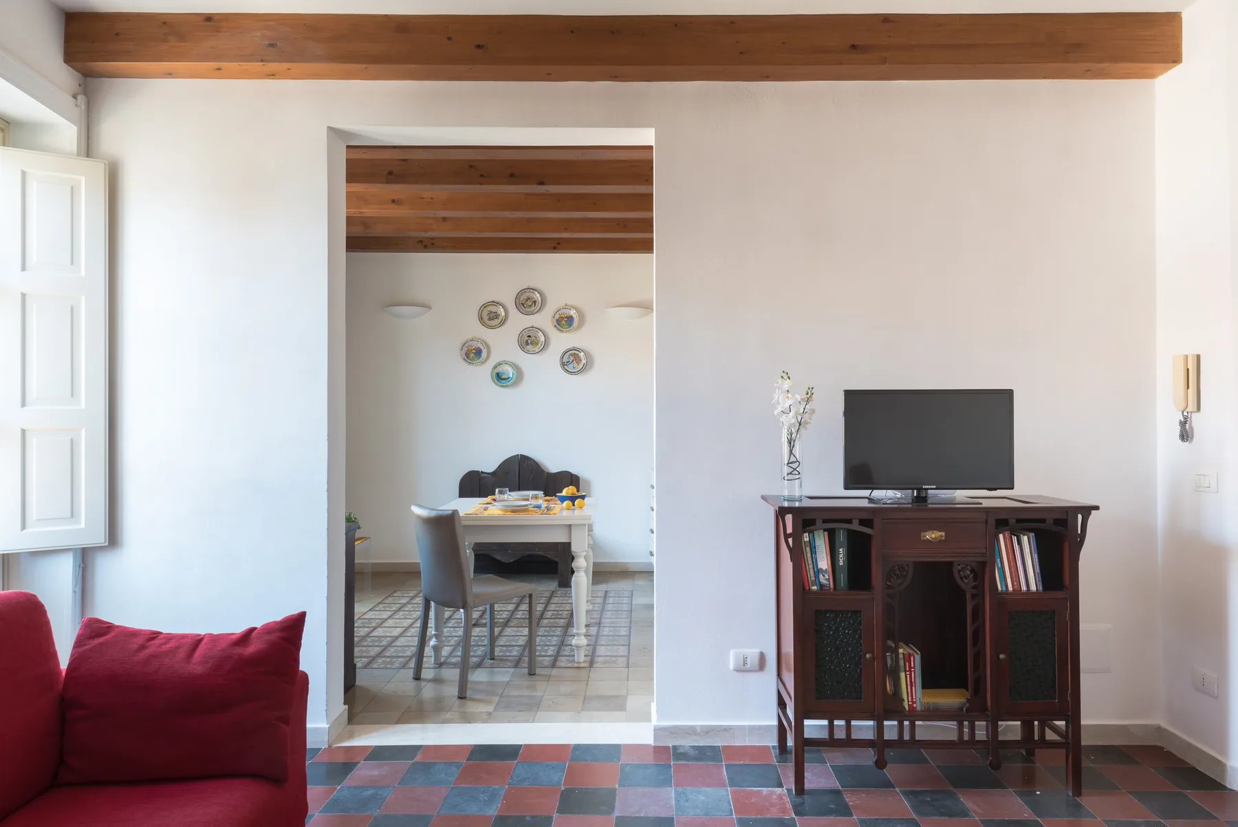 A living room with a television on a wooden cabinet and seating beside an open dining area.