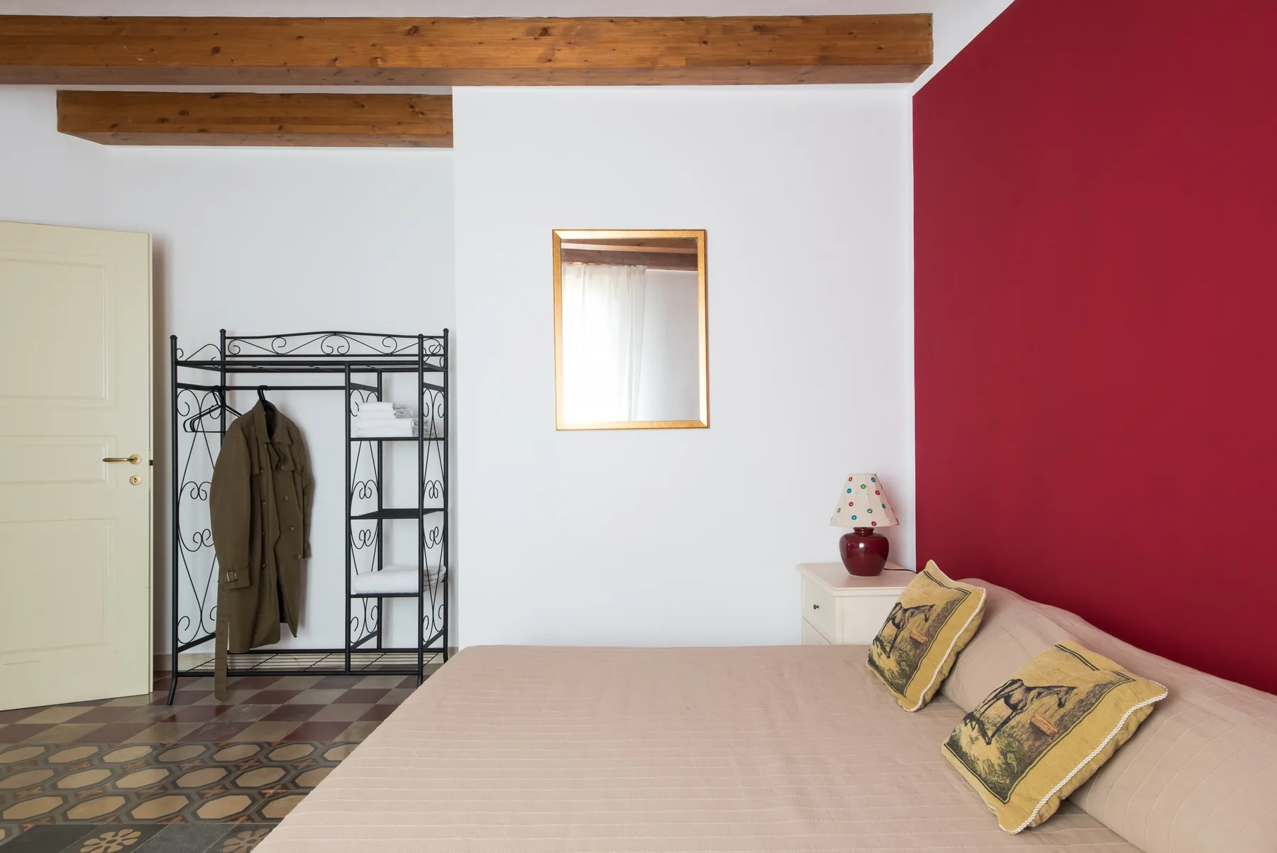 A bedroom with a bed against a red accent wall and a clothes rack nearby.