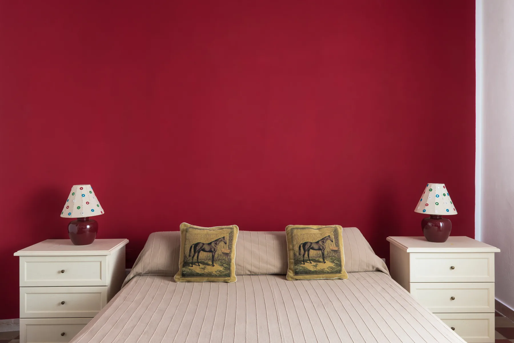 A bedroom with a bed against a deep red wall and matching bedside tables.