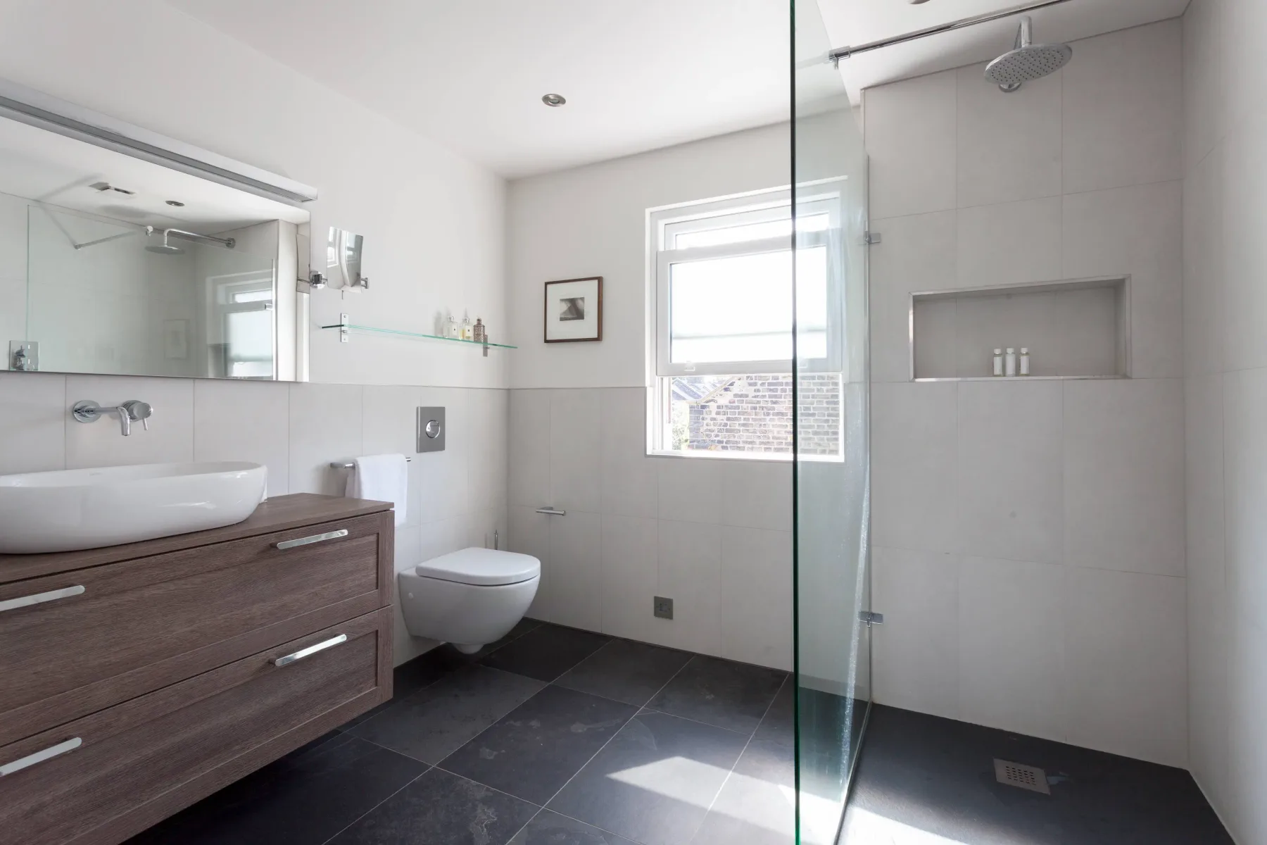 A bright bathroom with a vanity, toilet, and glass shower.