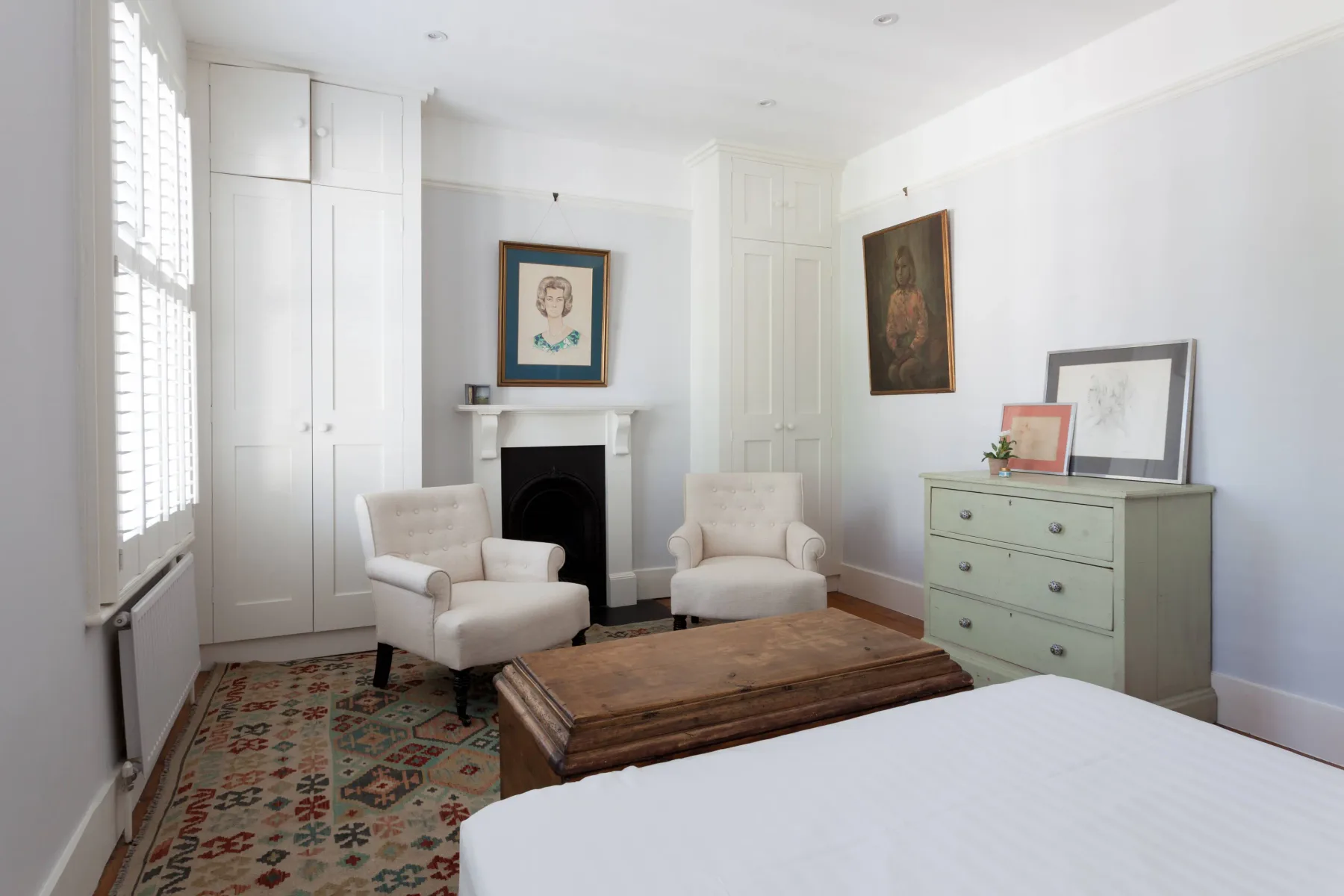A bright bedroom with seating around a fireplace and a dresser.