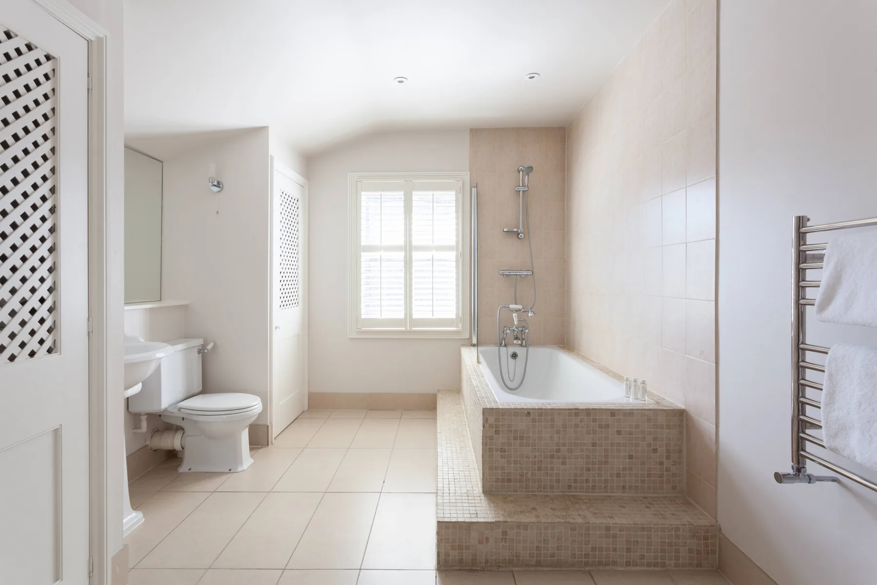 A bright tiled bathroom with a bathtub, shower, and window.
