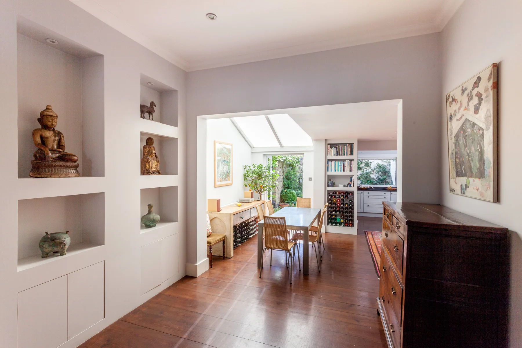 A dining area opens onto a bright kitchen with a table and built-in shelves.