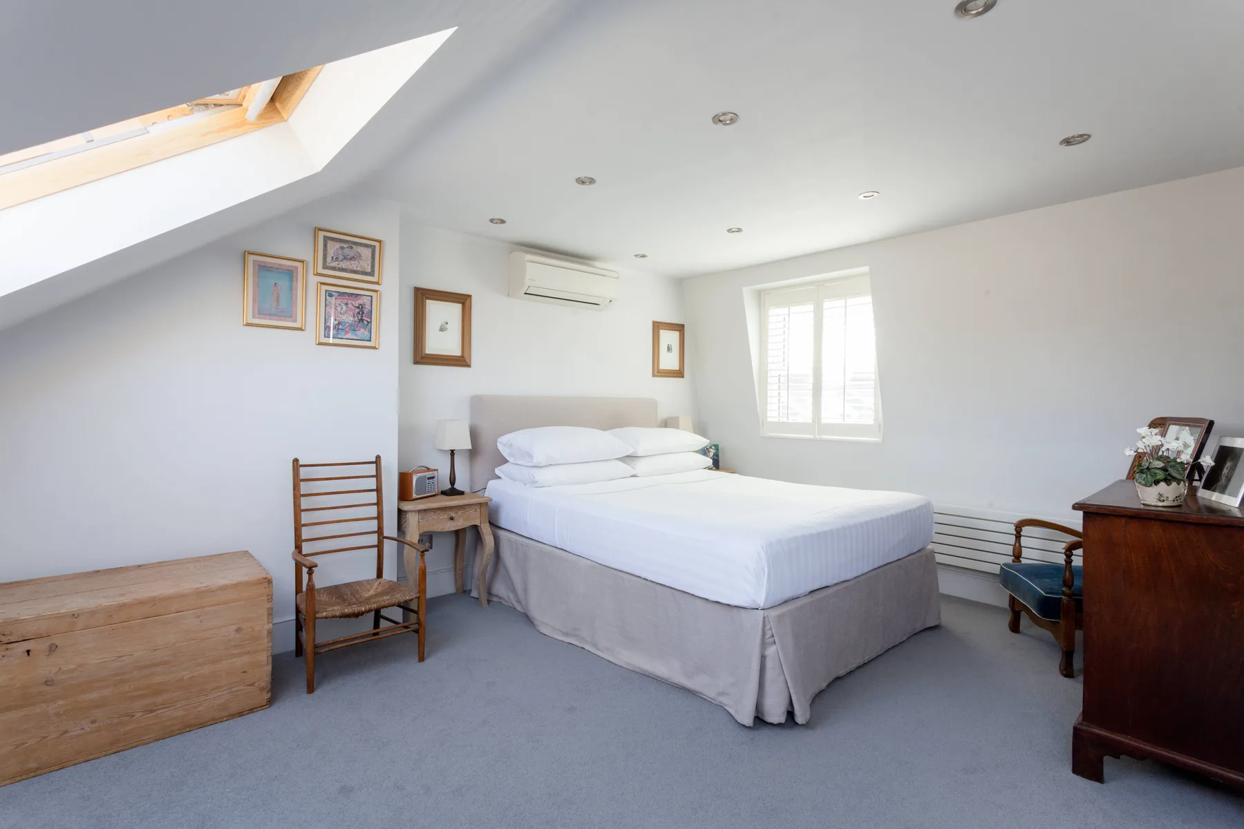 A bright attic bedroom with a neatly made bed and a skylight.