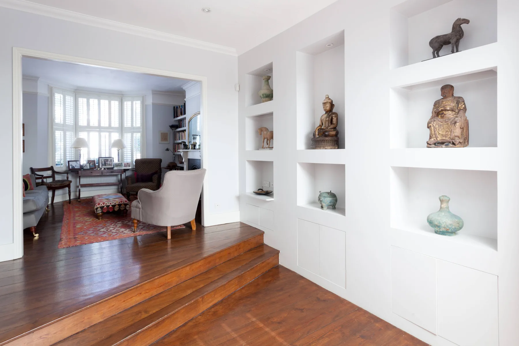 A bright living room with seating, a rug, and built-in display niches.