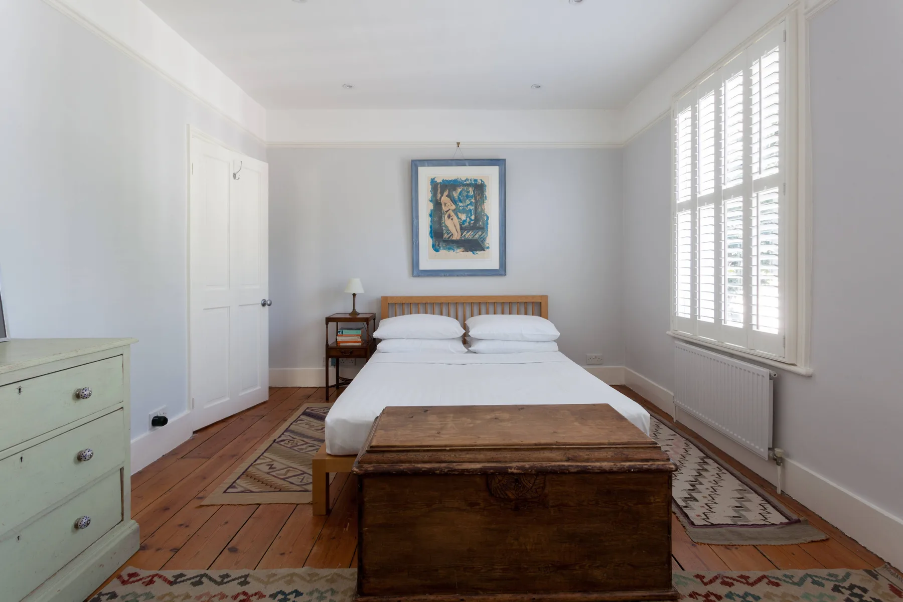A bedroom with a bed, wooden chest, and large shuttered windows.