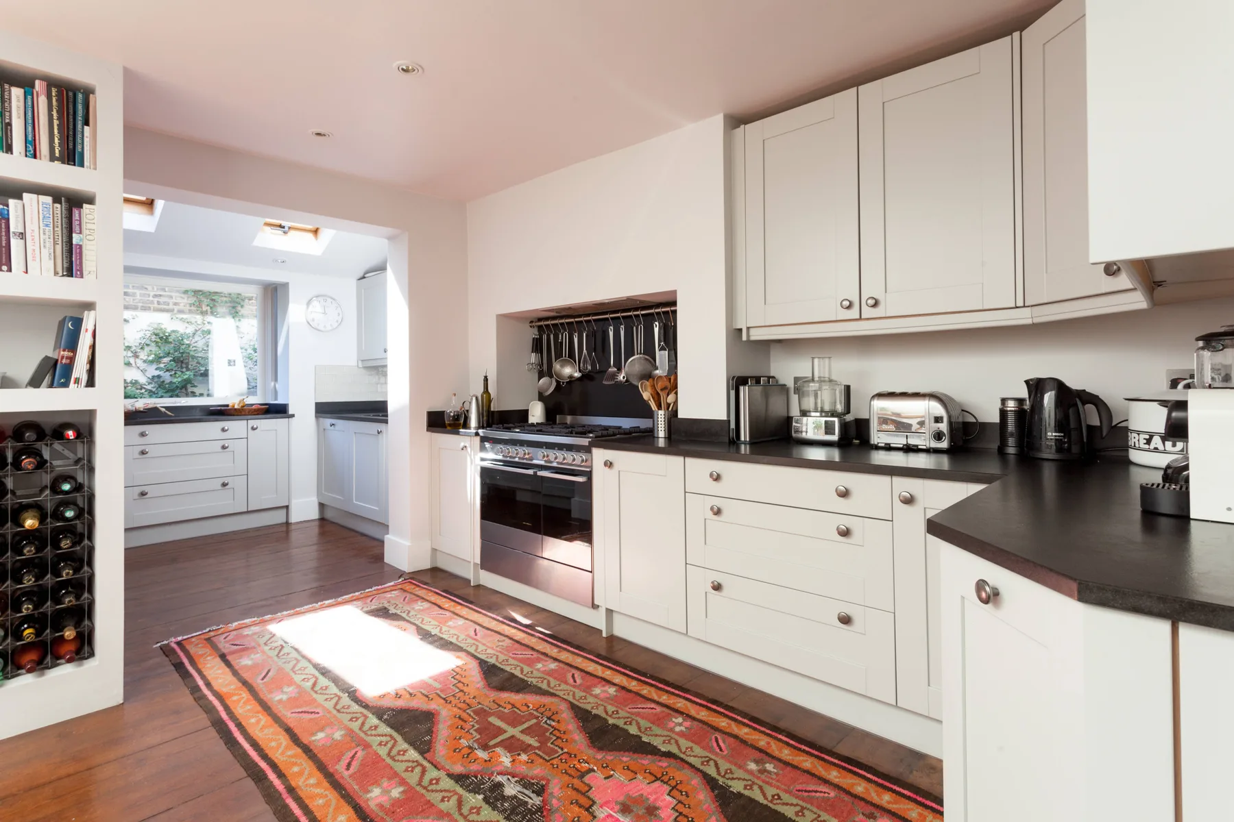 A bright kitchen with dark countertops, white cabinets, and a patterned rug.
