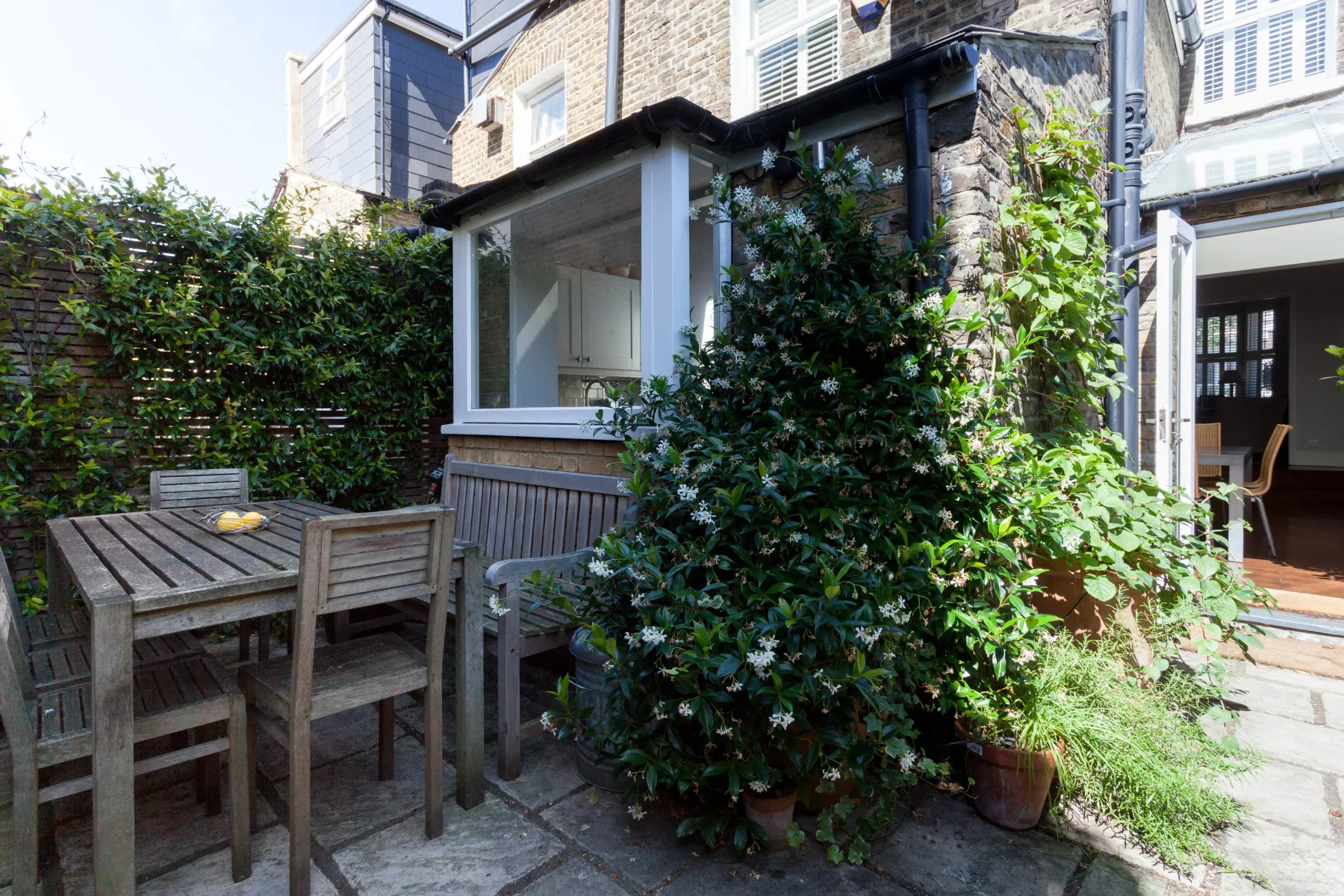 A paved patio with outdoor seating and abundant greenery beside the house.