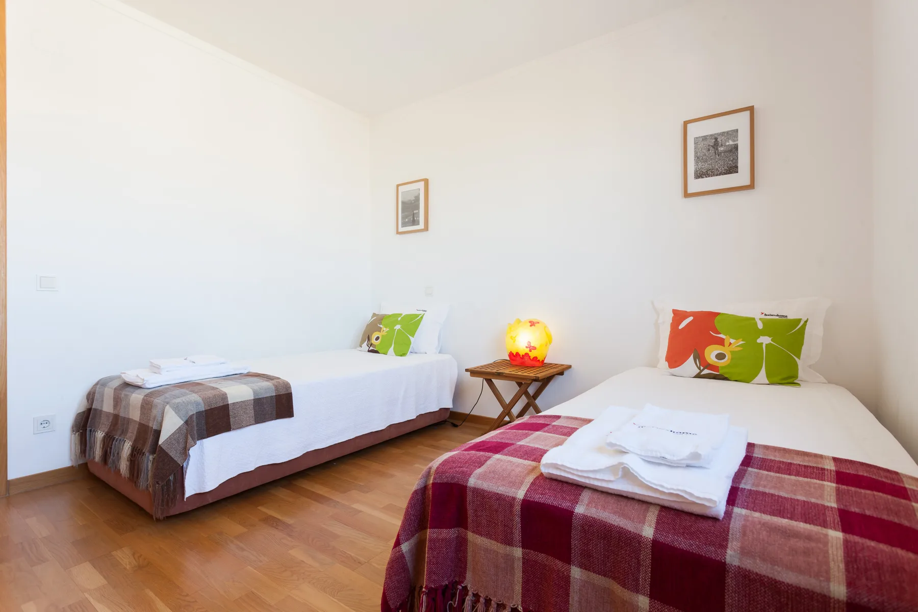 Un dormitorio luminoso con dos camas, mantas estampadas y una mesita entre ellas.