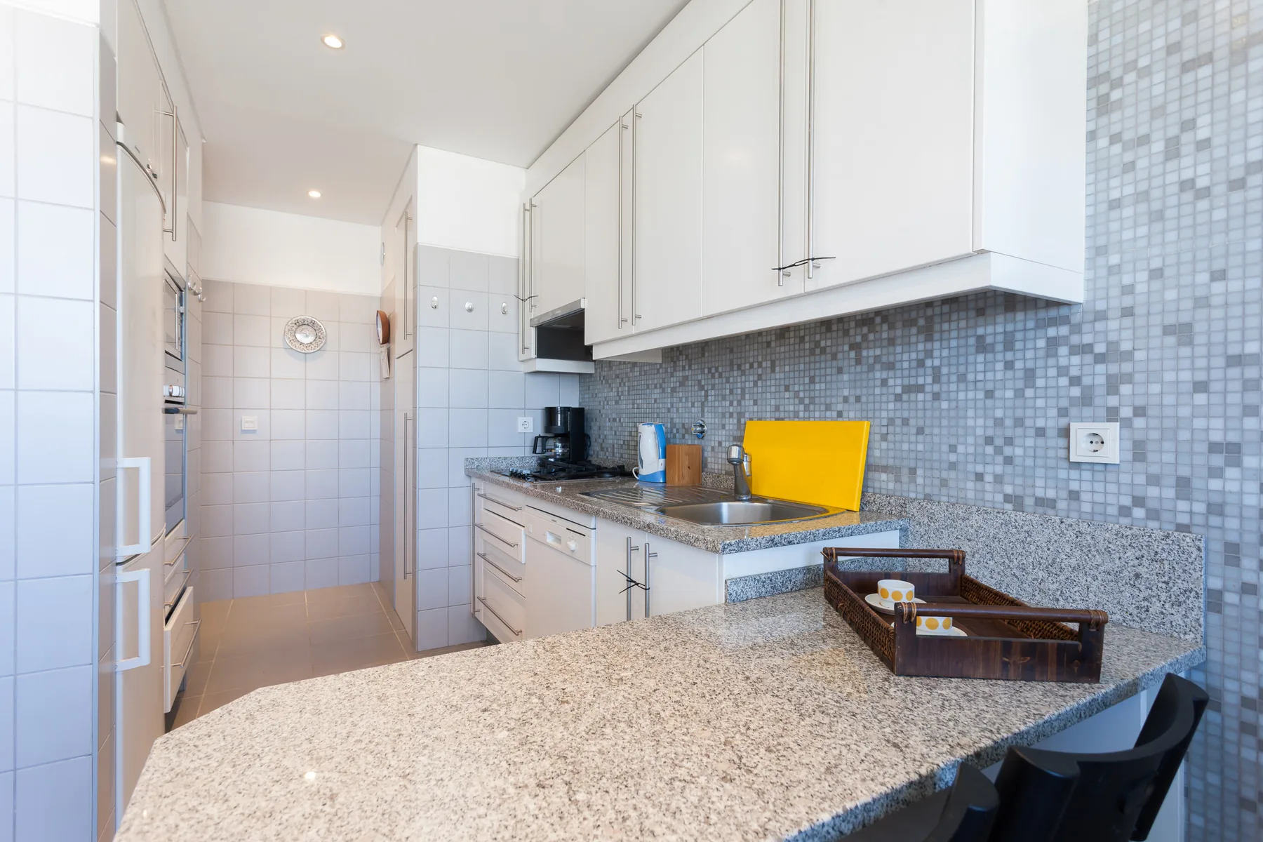 A bright kitchen with a long countertop and white cabinets.