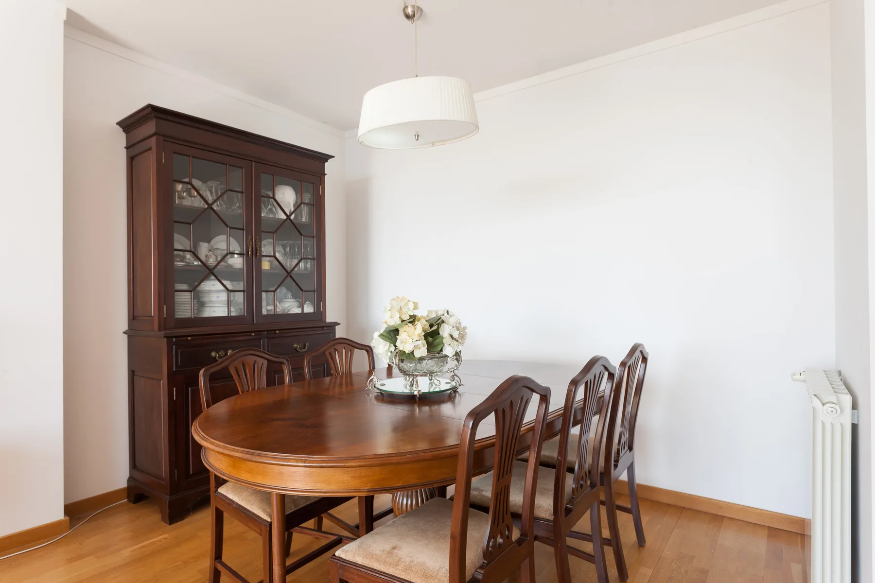 A dining area with a wooden table, chairs, and a glass-front cabinet.