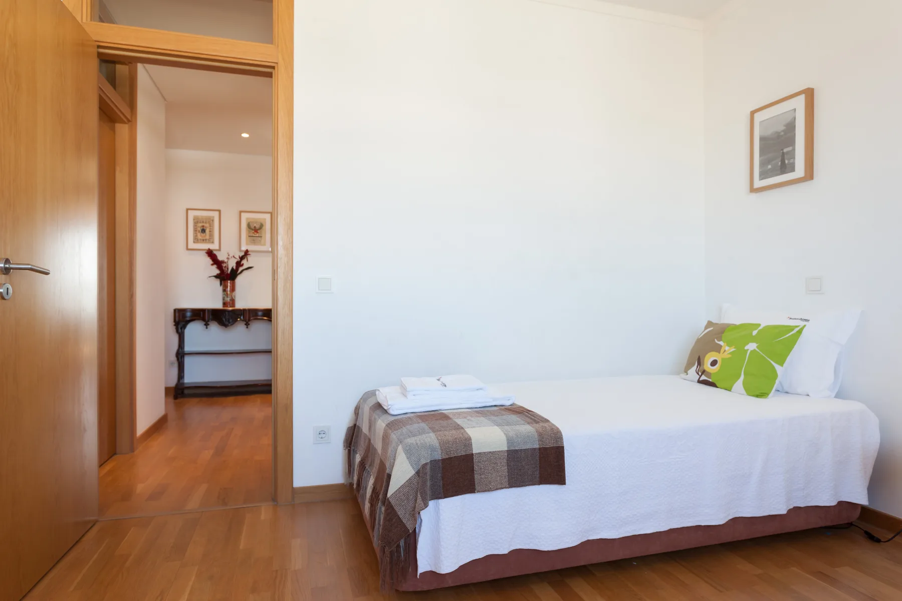 A bedroom with a bed, folded linens, and a green accent pillow.