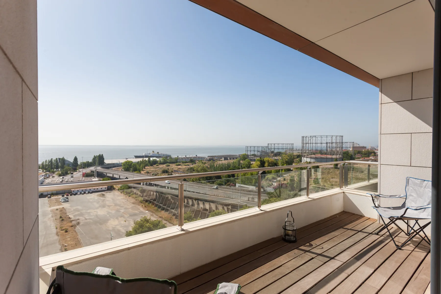 A balcony with glass railing overlooks a broad urban landscape and the water.